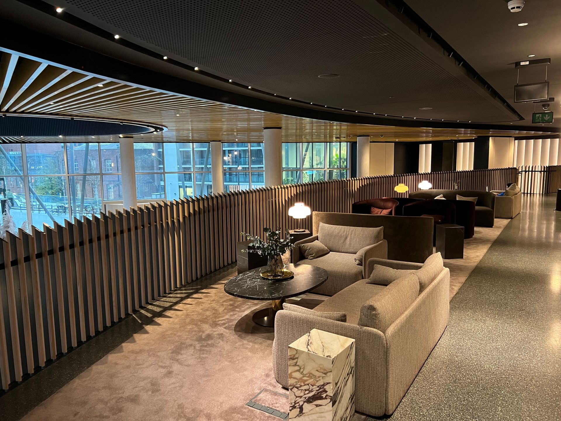 Lounge area with light-colored sofas, dark coffee table, and patterned ceiling. Wooden screen separates from outside view.