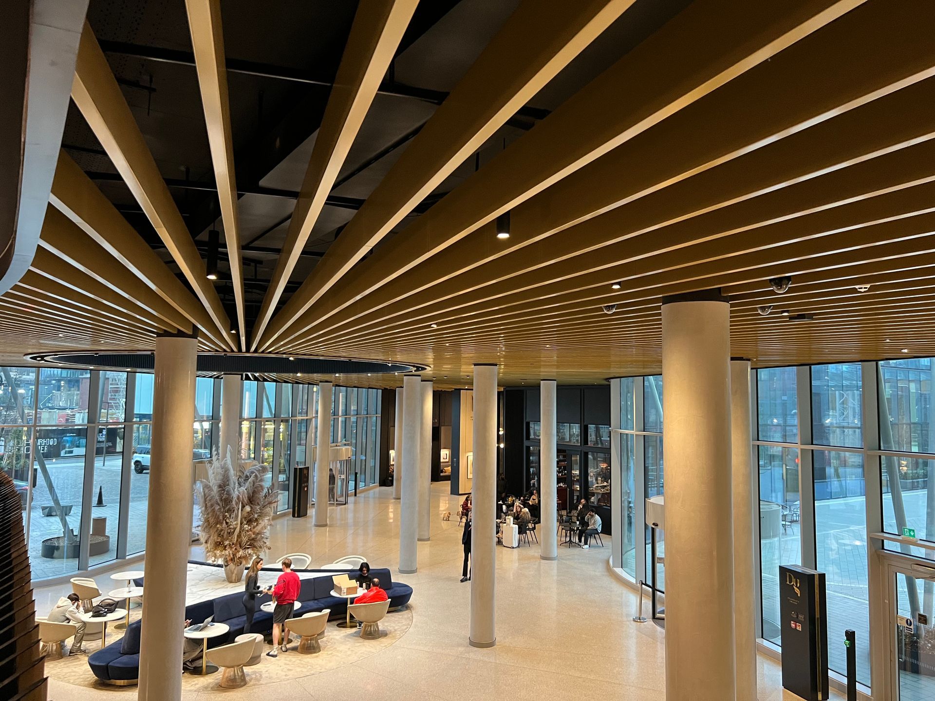 Interior view of a modern building lobby with a unique gold ceiling design, columns, and large windows. People are present.