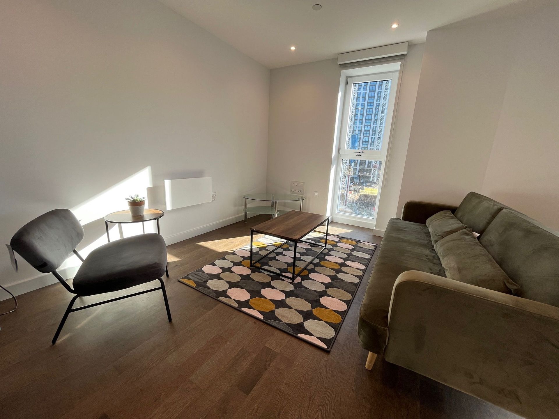 Living room with green sofa, gray chair, patterned rug, and large window.