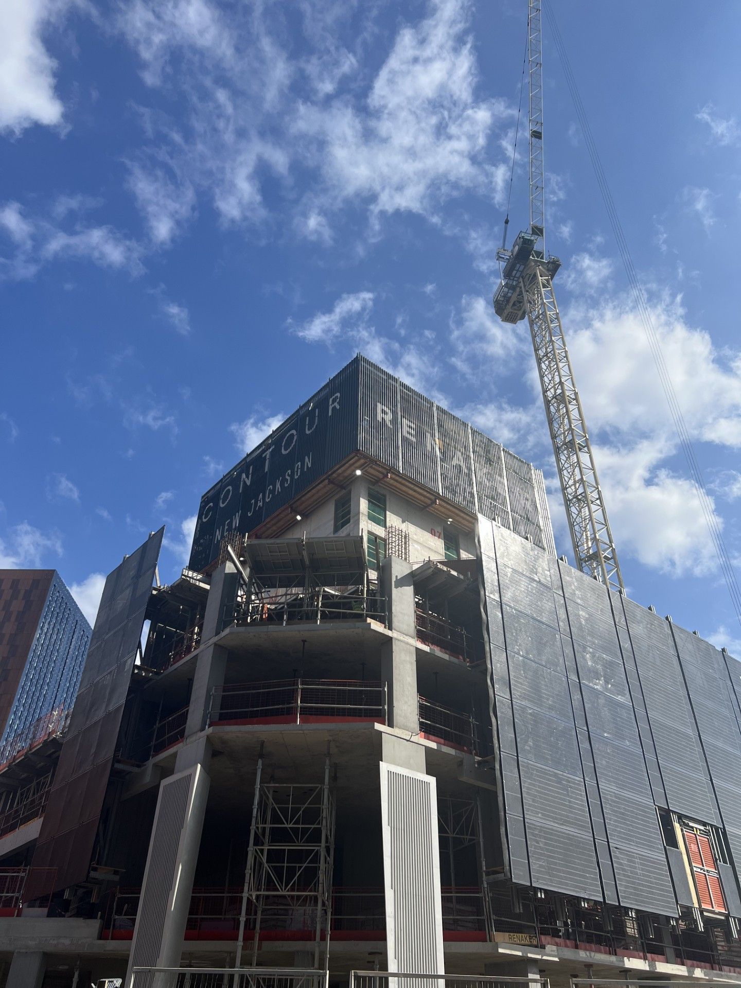 Building under construction with a crane against a blue sky. Exterior with scaffolding and dark panels.