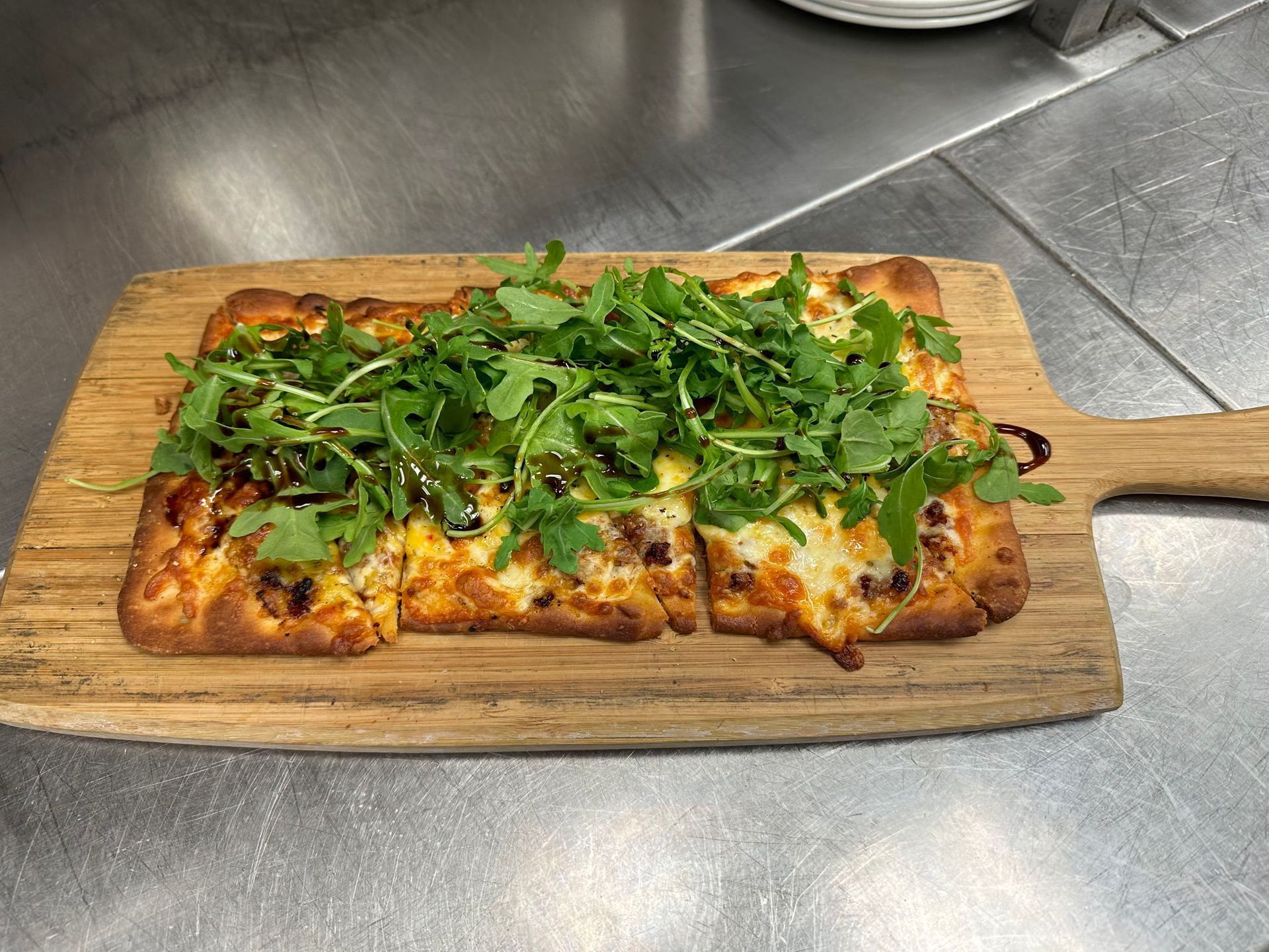 Pizza with arugula on a wooden board, served on a stainless steel surface.