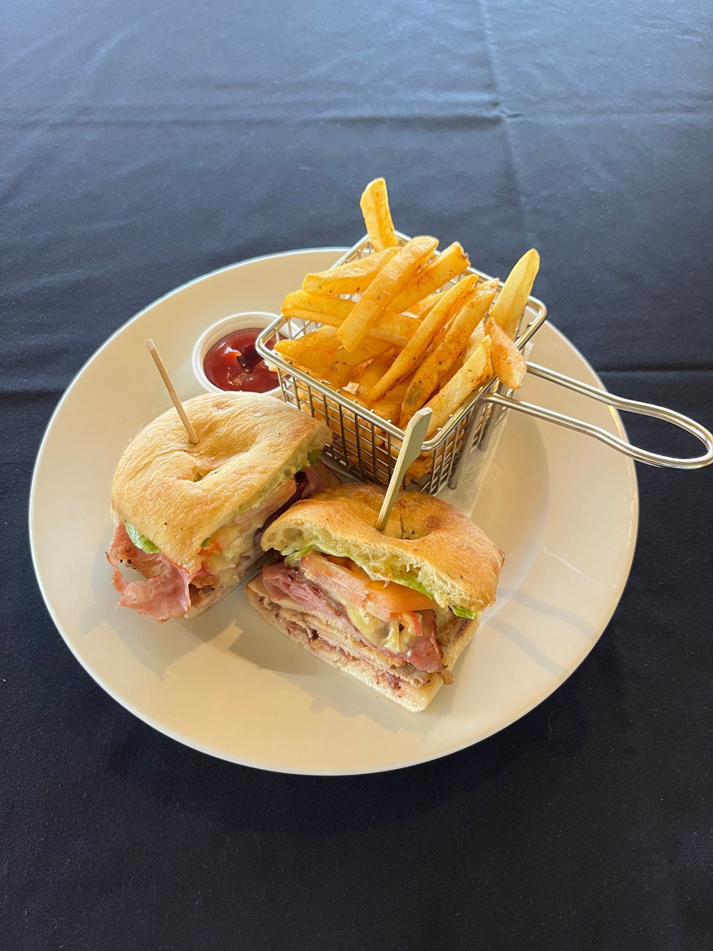 Woman behind a counter holds two canned drinks, smiling. Restaurant setting with food display, windows.