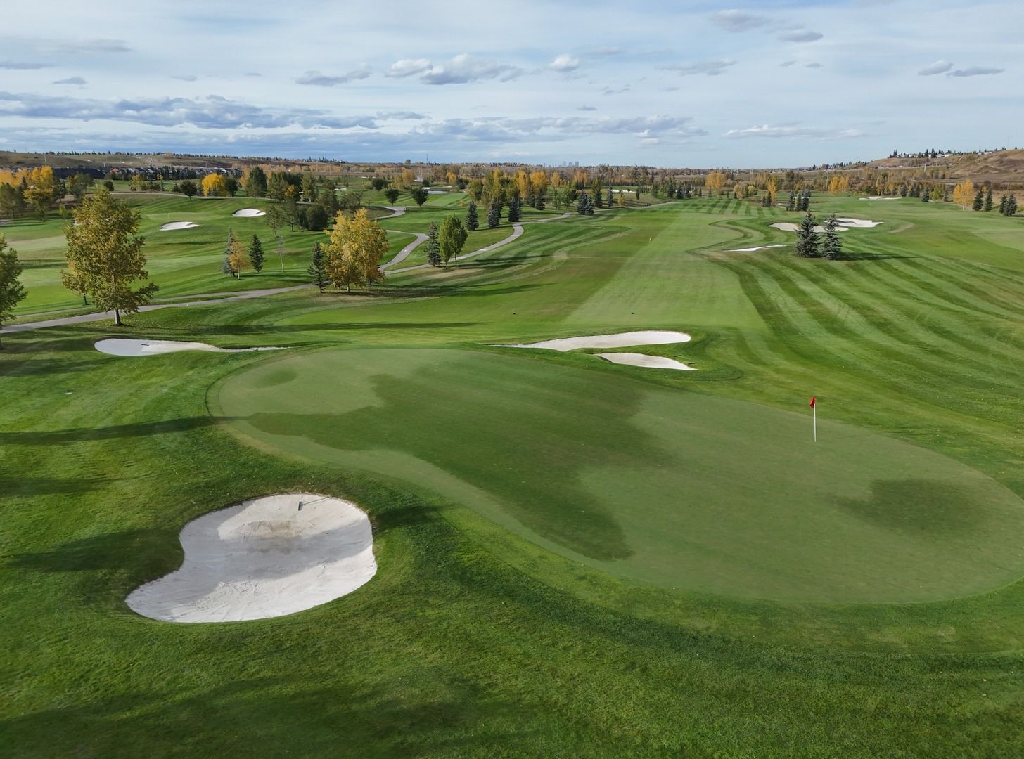 Green golf course with sand traps and trees under a cloudy sky.
