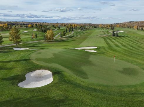 Green golf course with sand traps and trees under a cloudy sky.