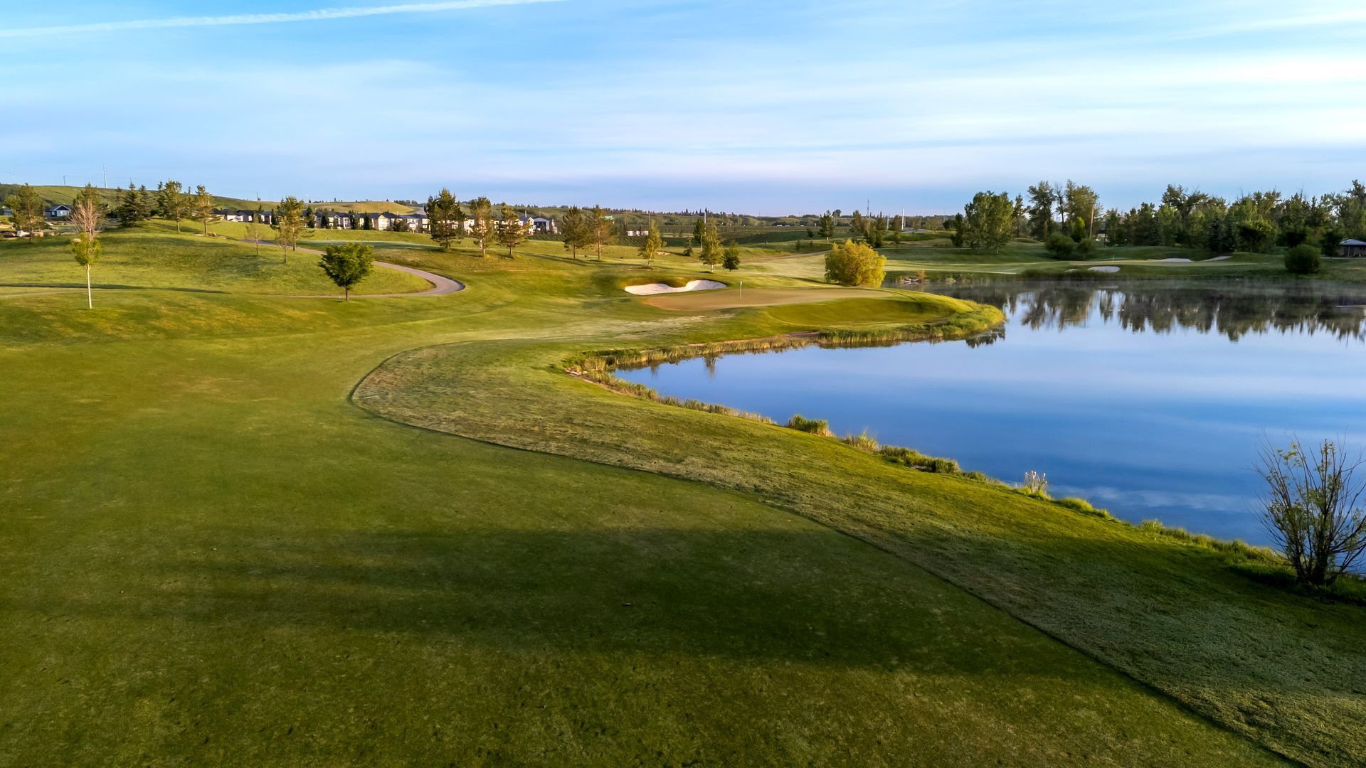Green golf course with a lake and blue sky.