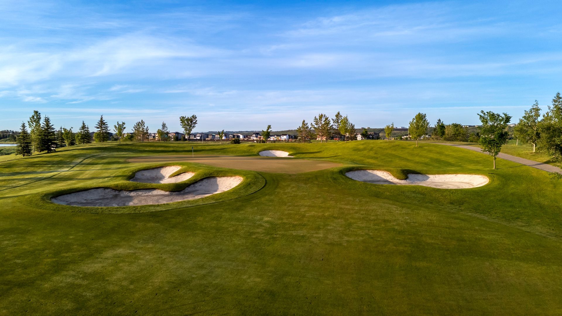 Golf course with green grass, sand traps, and trees under a blue sky.