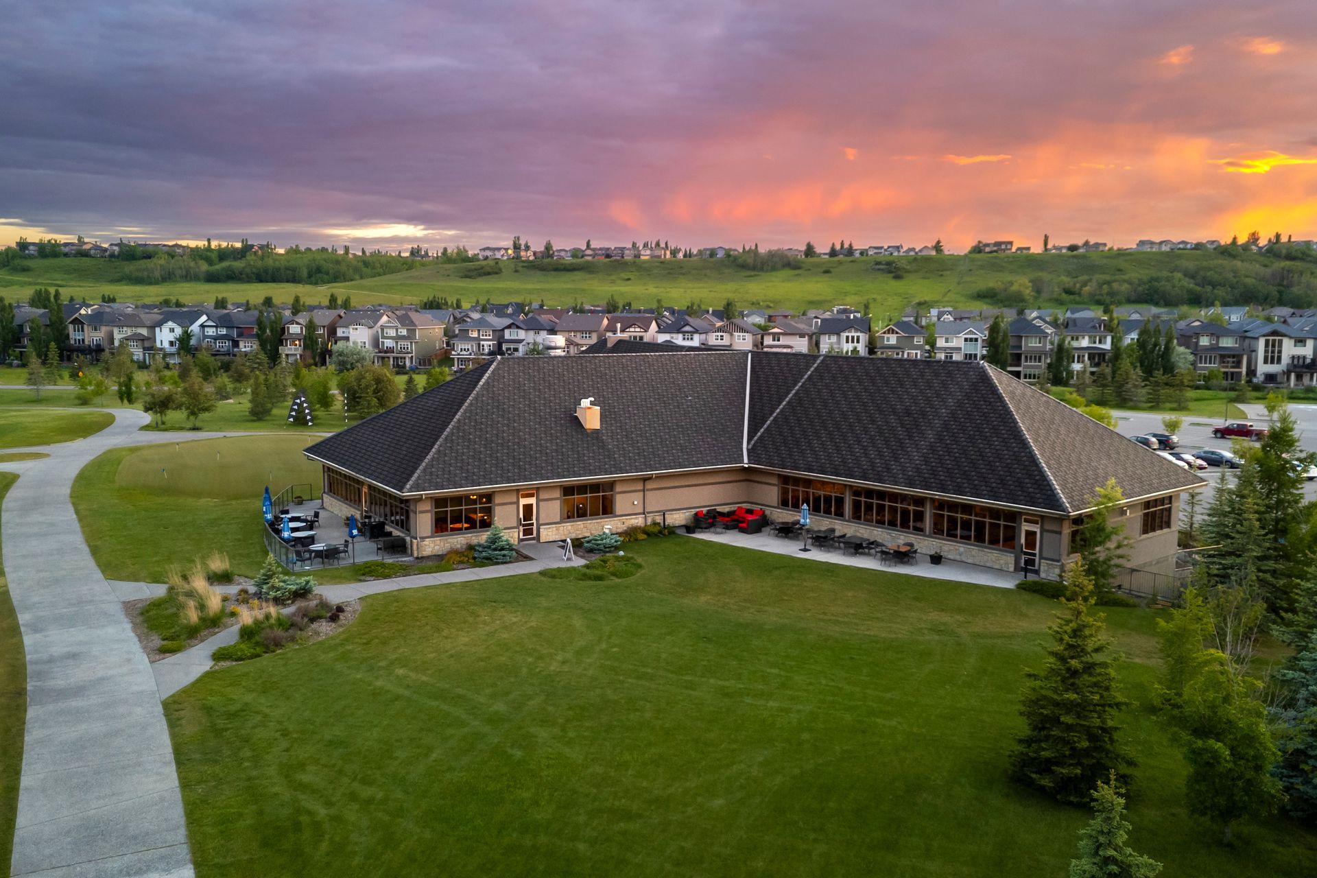 Clubhouse on a golf course with green grass, walkway, and sunset sky.