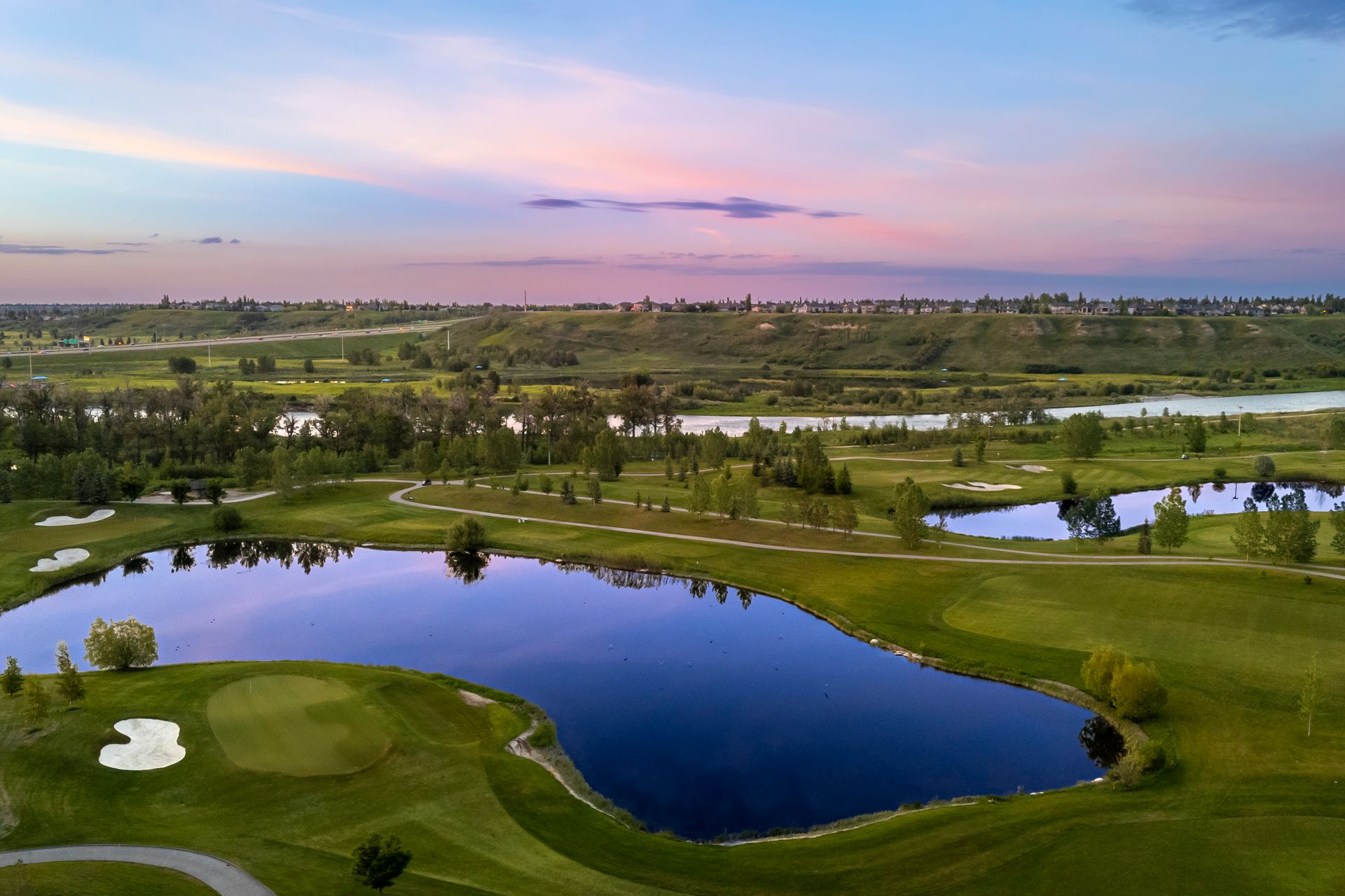 Aerial view of a golf course with a lake and sunset sky.