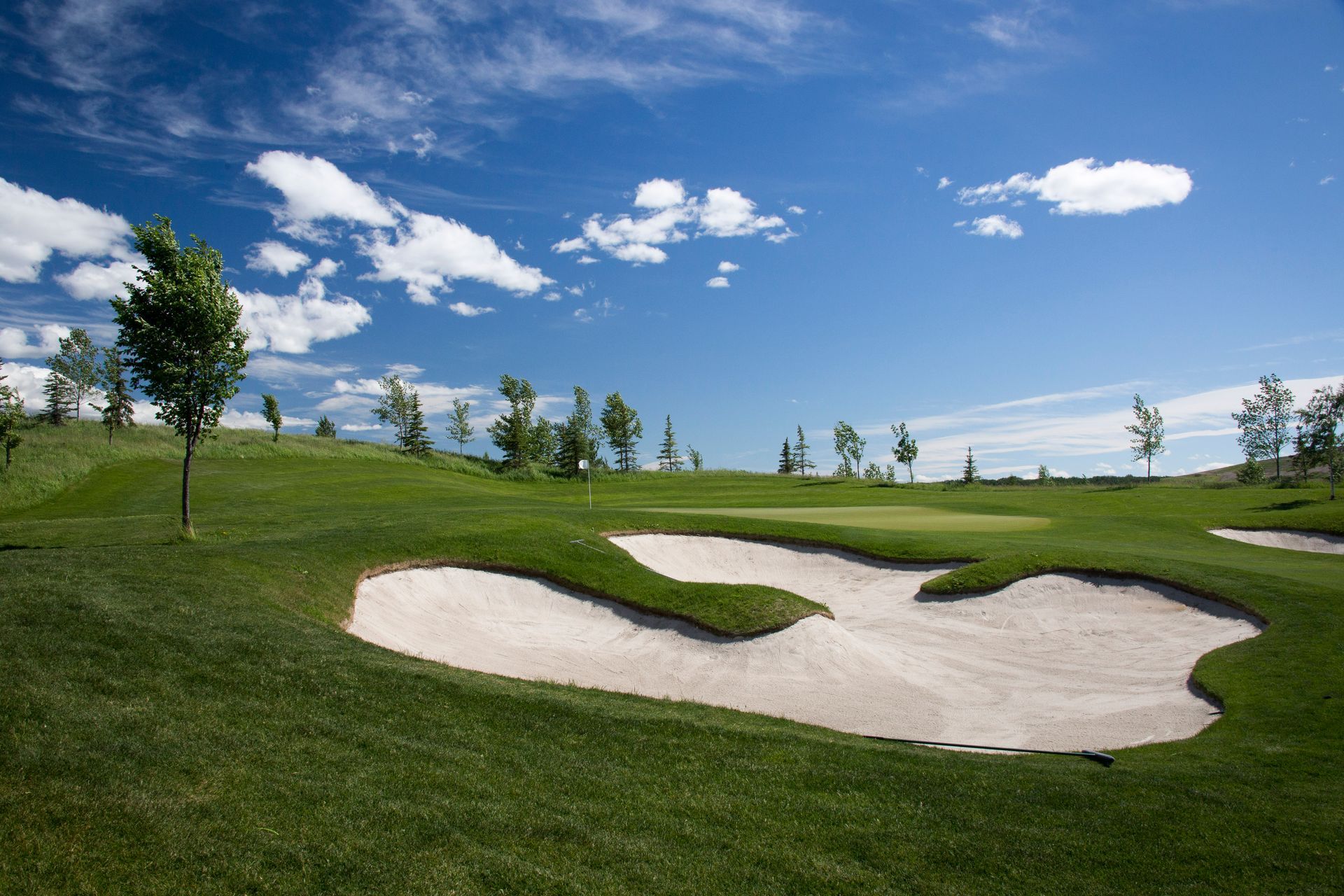 Golf course green with sand trap, blue sky, and scattered clouds.