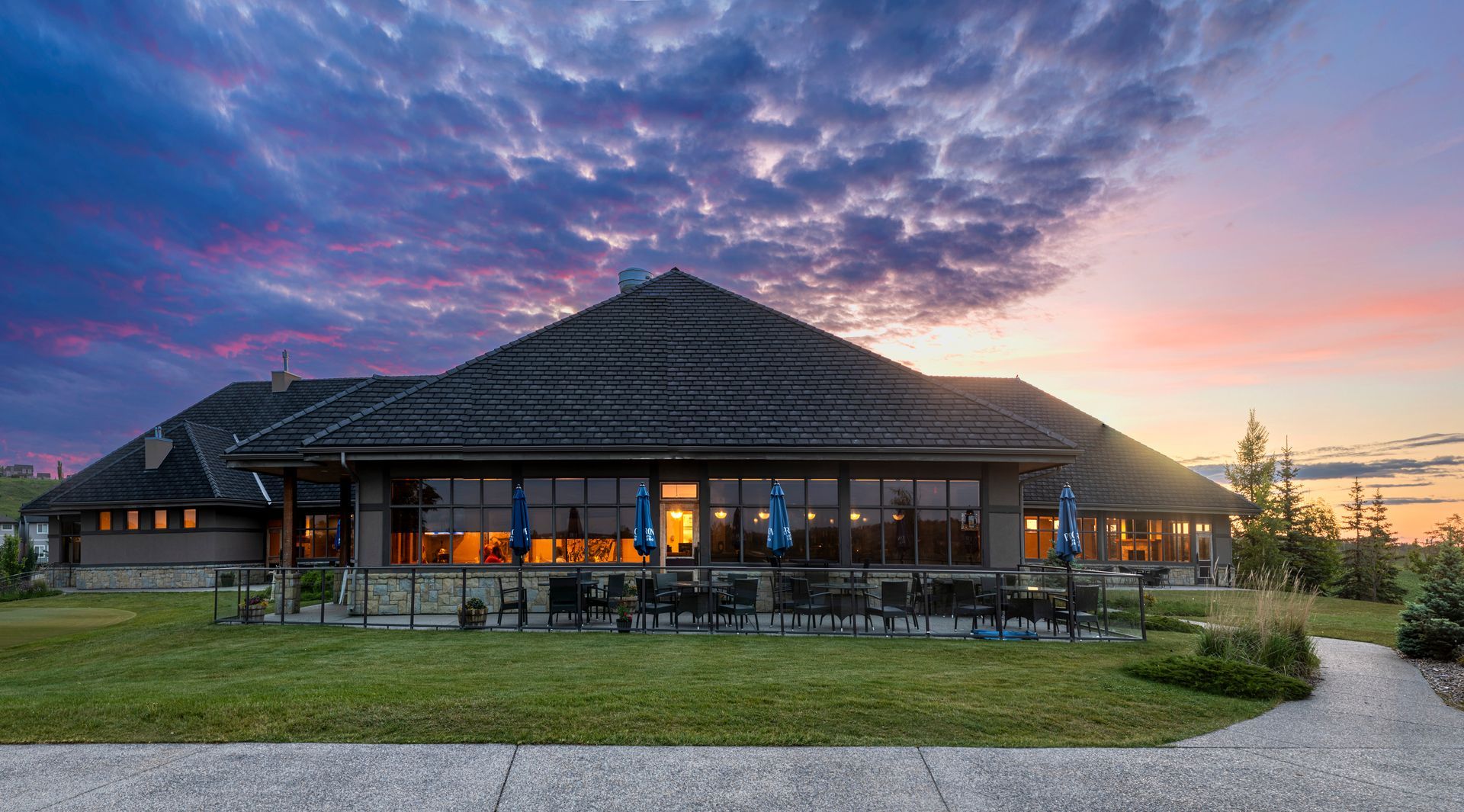 Building with shaded outdoor seating, overlooking a green golf course. People under blue umbrellas.