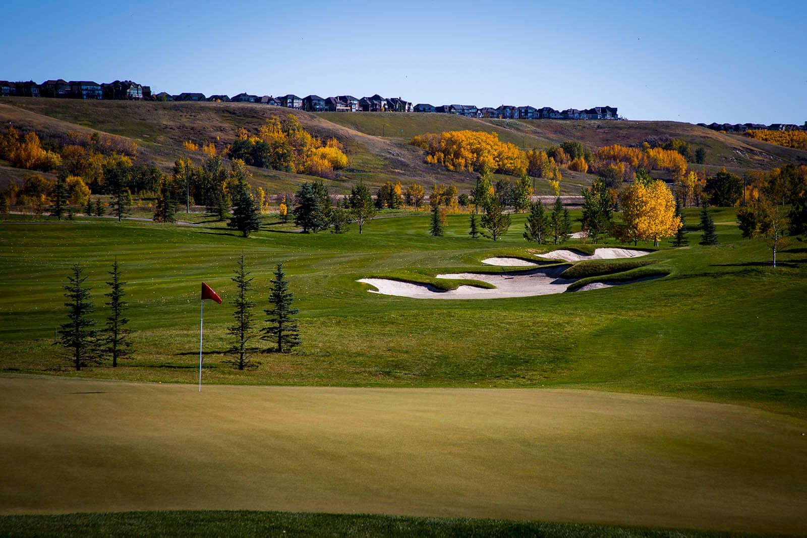 Golf course with green grass, bunkers, and fall foliage; red flag on the green.