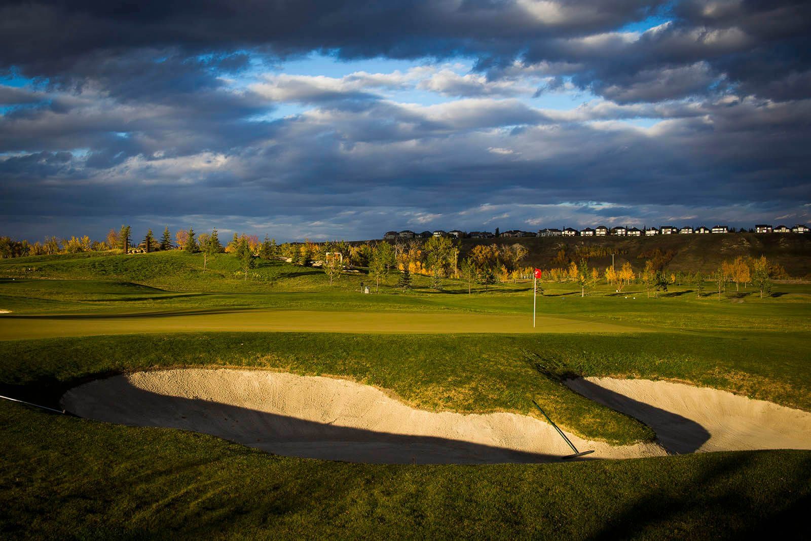 Golf course scene with green grass, sand trap, and cloudy sky.