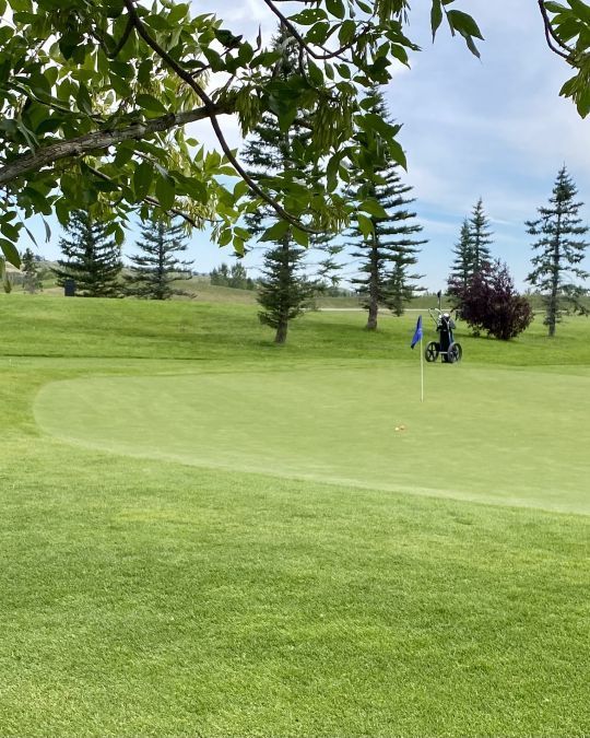 A golf course with a small motorized cart tending the green on a sunny day.