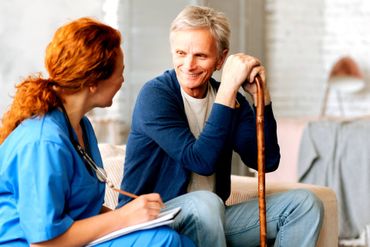 A nurse is talking to an elderly man with a cane.