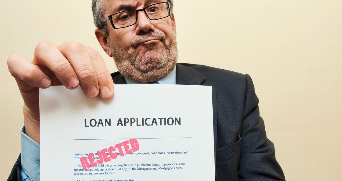 A man is holding up a loan application that has been rejected