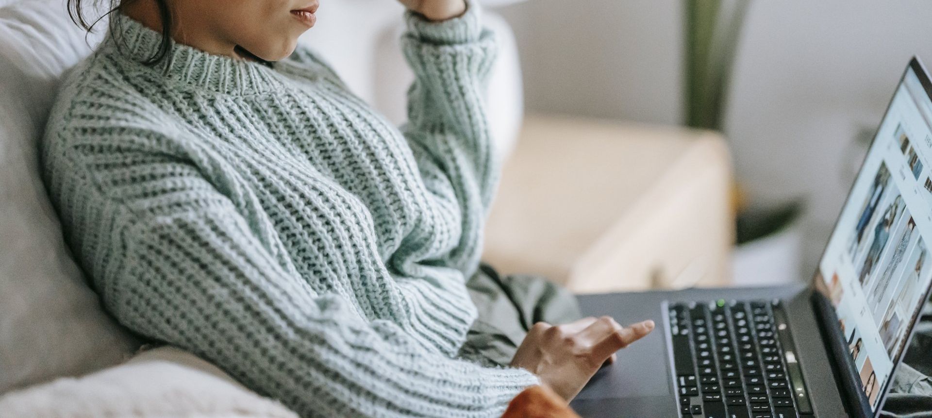 A woman is sitting on a couch using a laptop computer.