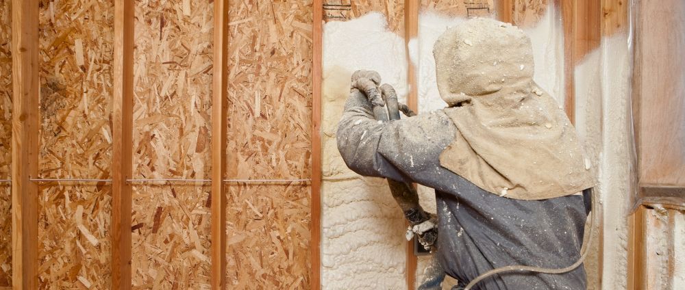 A man is spraying insulation on a wooden wall.