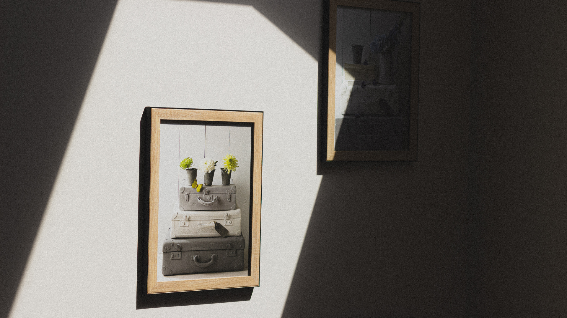 A picture of a suitcase with flowers in it is hanging on a wall.