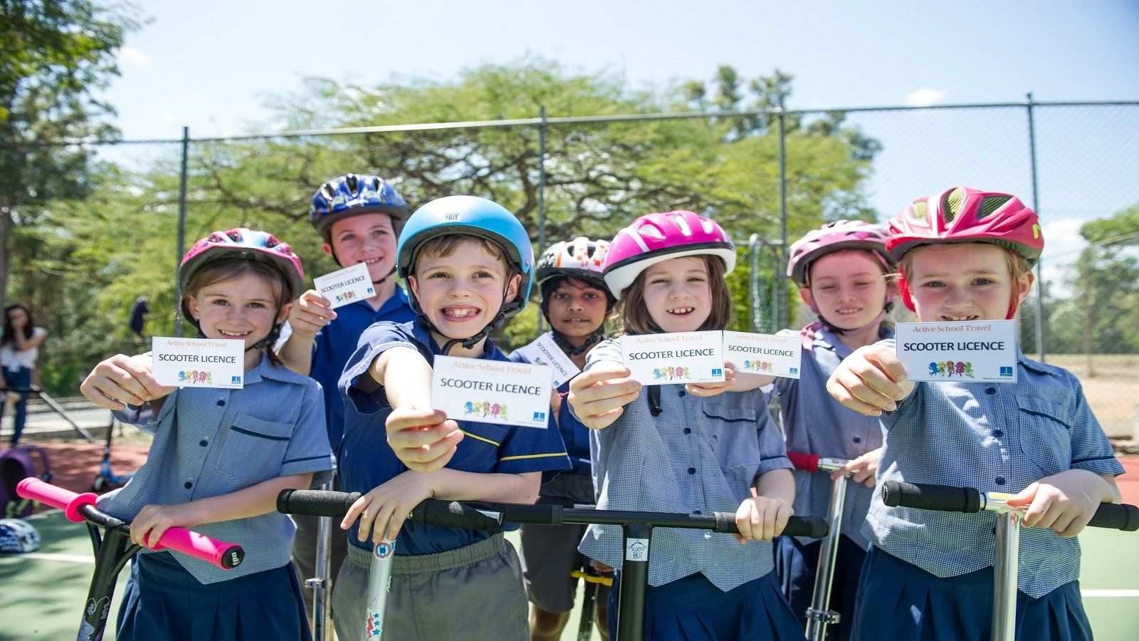 A group of children wearing helmets and scooters are holding up signs.