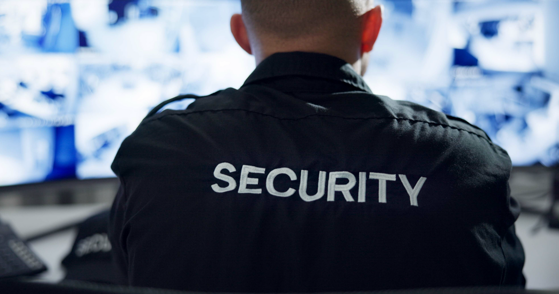 A security guard is sitting in front of a computer monitor.