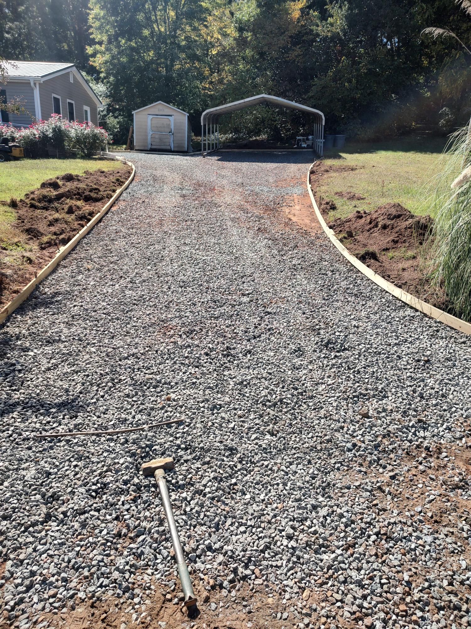 A gravel driveway leading to a house with a shed in the background.