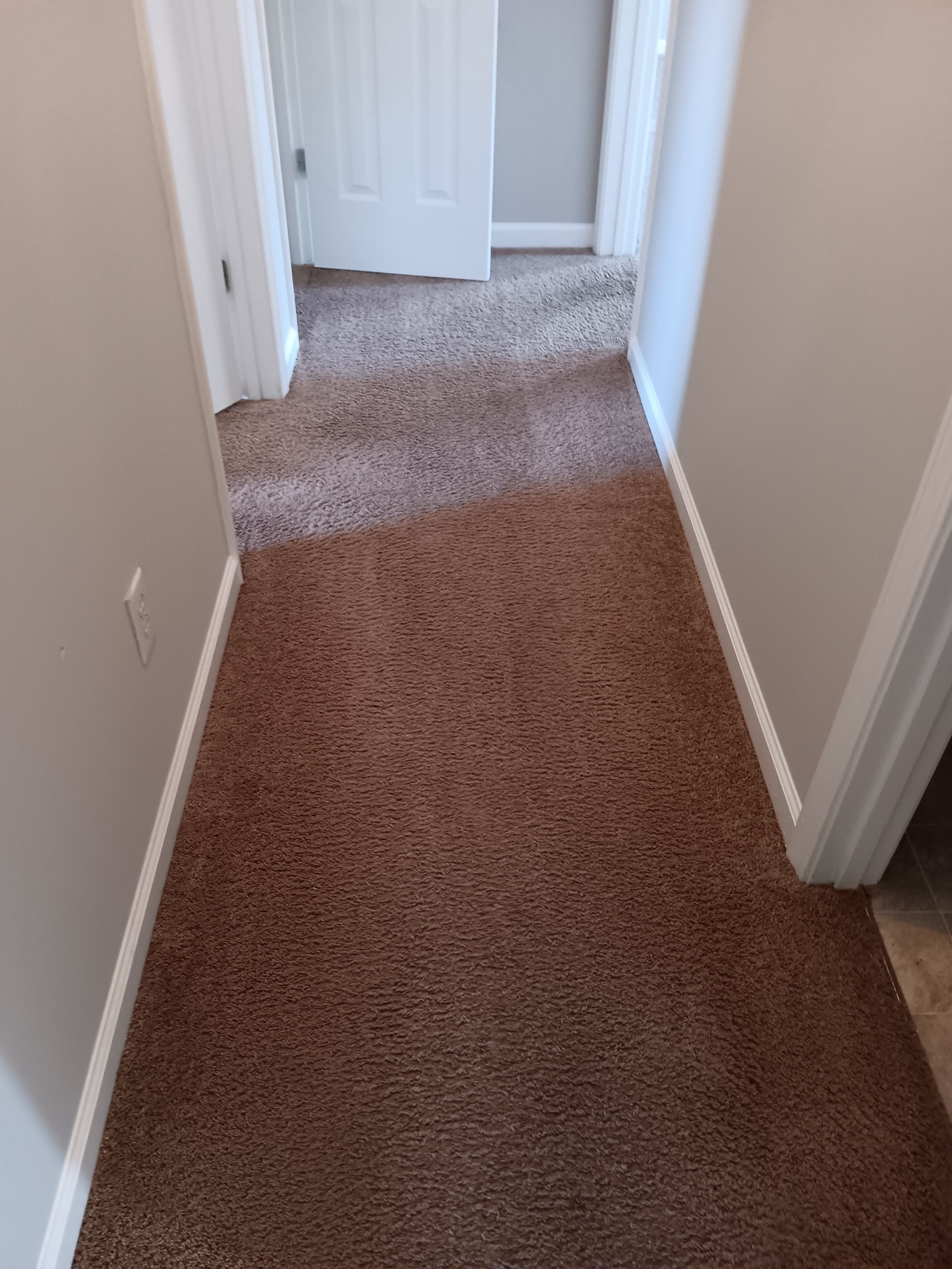 Narrow hallway with brown carpet, neutral walls, and white trim; doors open at each end.