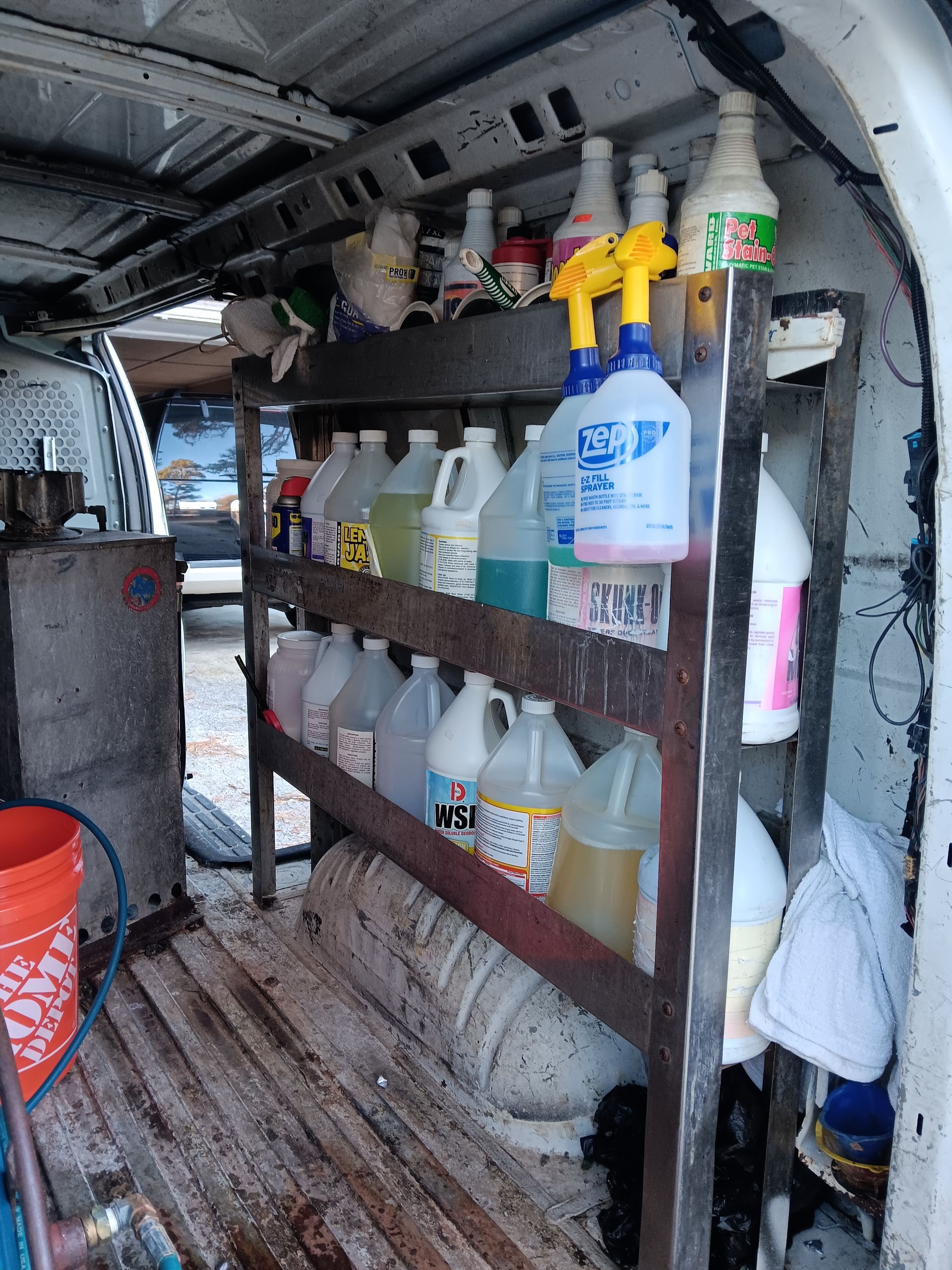 Inside a work van, a metal shelf holds various cleaning product bottles.