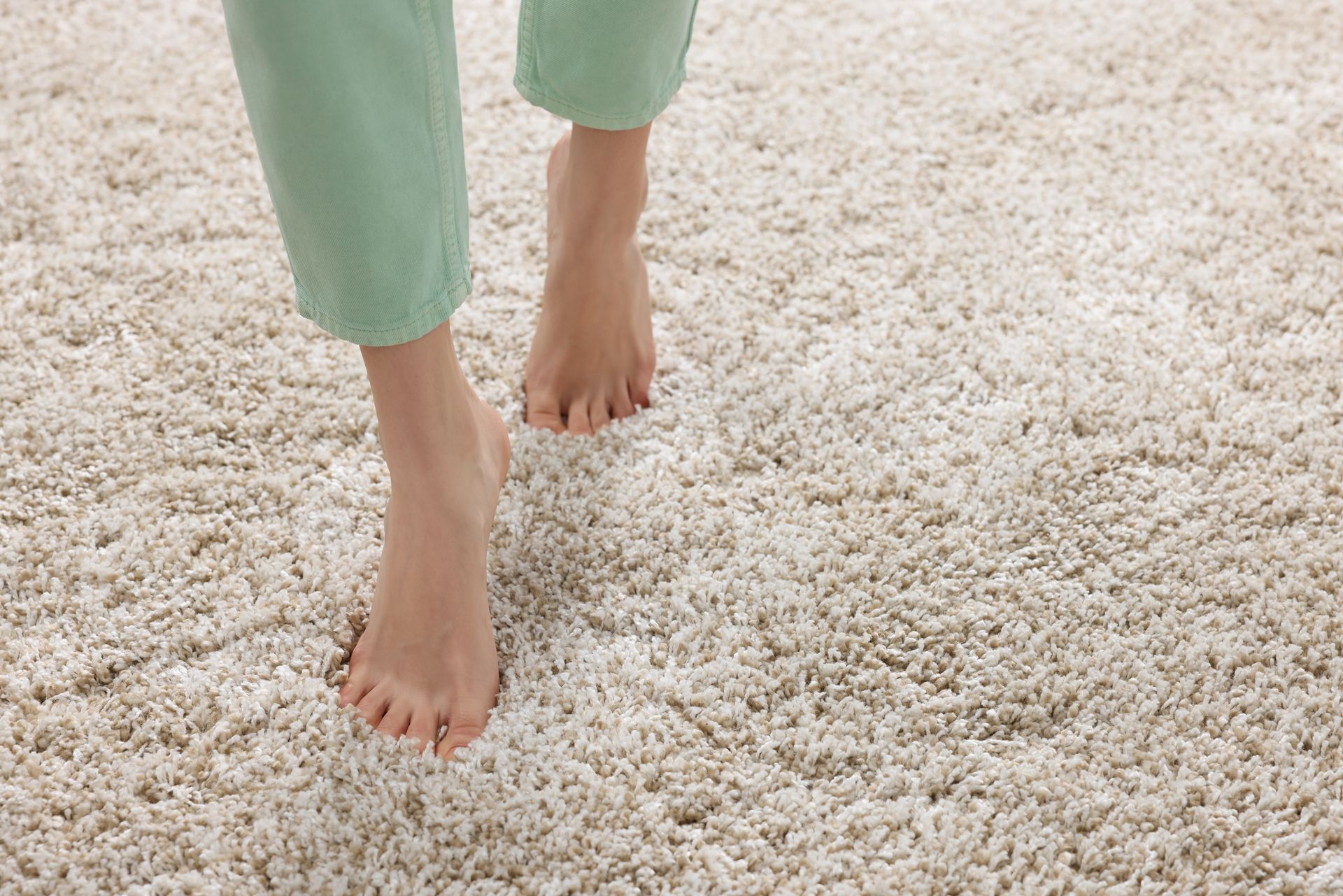 Bare feet walking on a plush, cream-colored carpet; green pants visible.