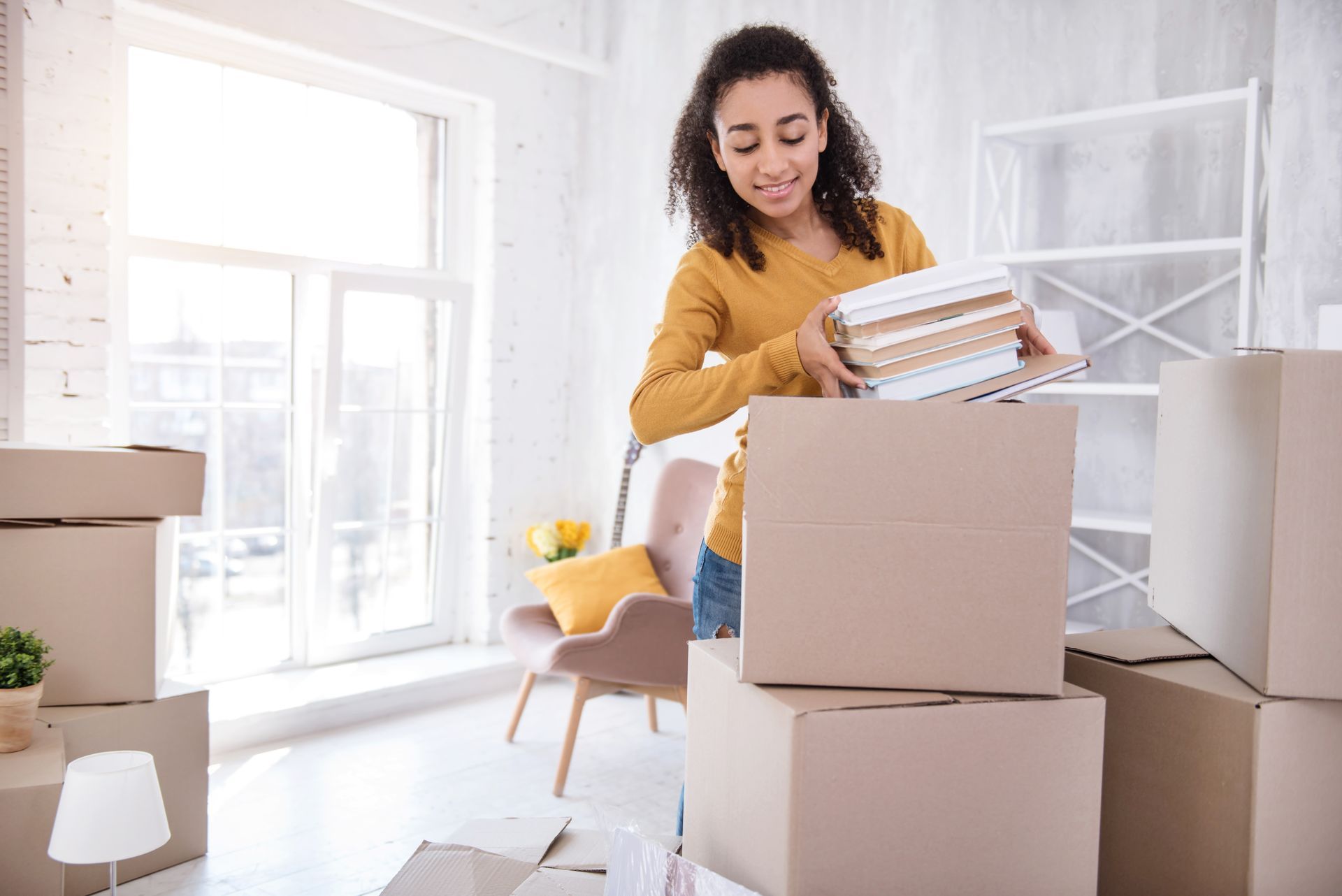 A young woman packing books into a box in preparation for her apartment move.