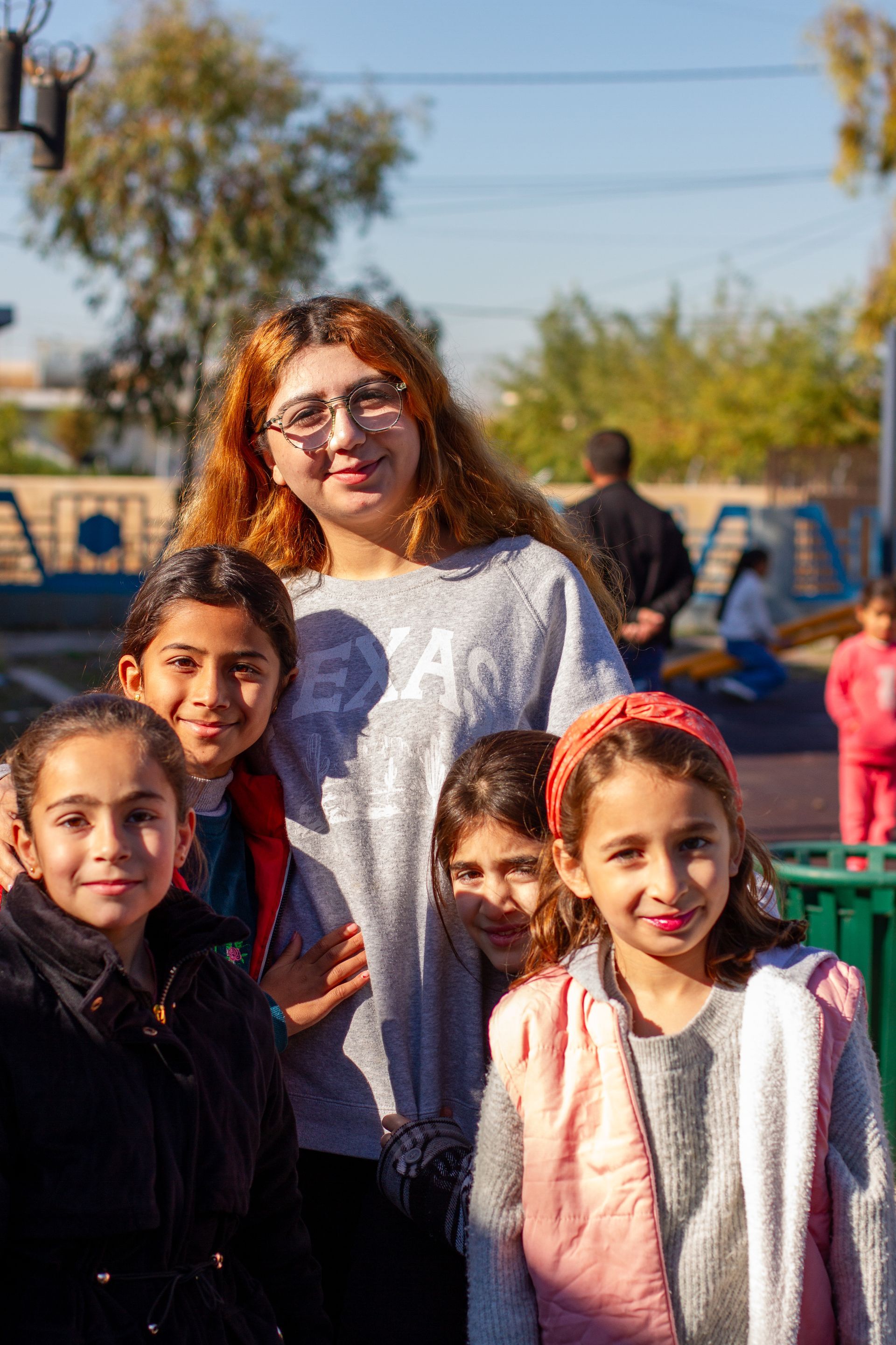 Group of people standing outdoors, some children. One person in a patterned shirt.