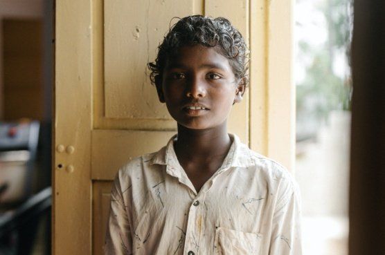 Young person in a light-colored button-up shirt standing in front of a yellow door.