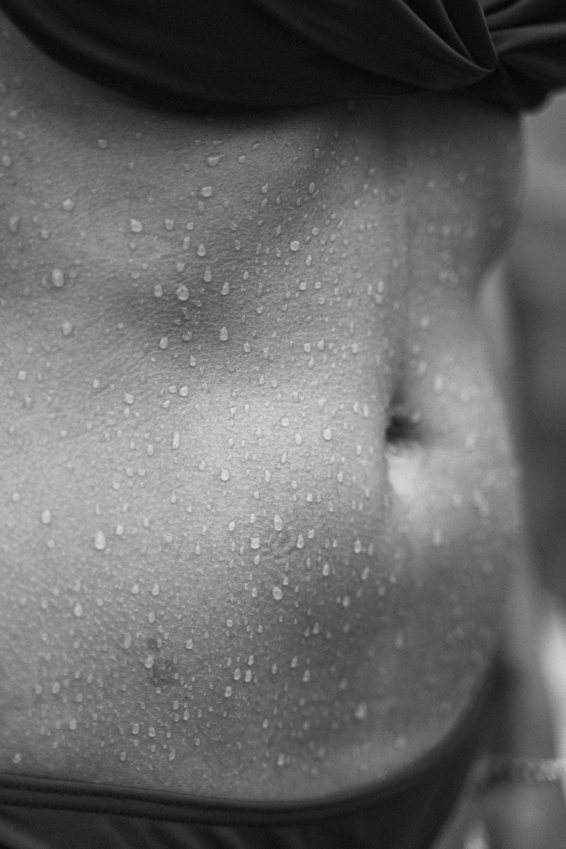 A black and white photo of a woman 's stomach with water drops on it.