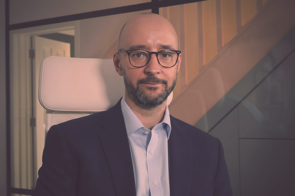Justin Tate of The Exec Memo  wearing glasses and suit, looking at the camera. He's in an office setting.