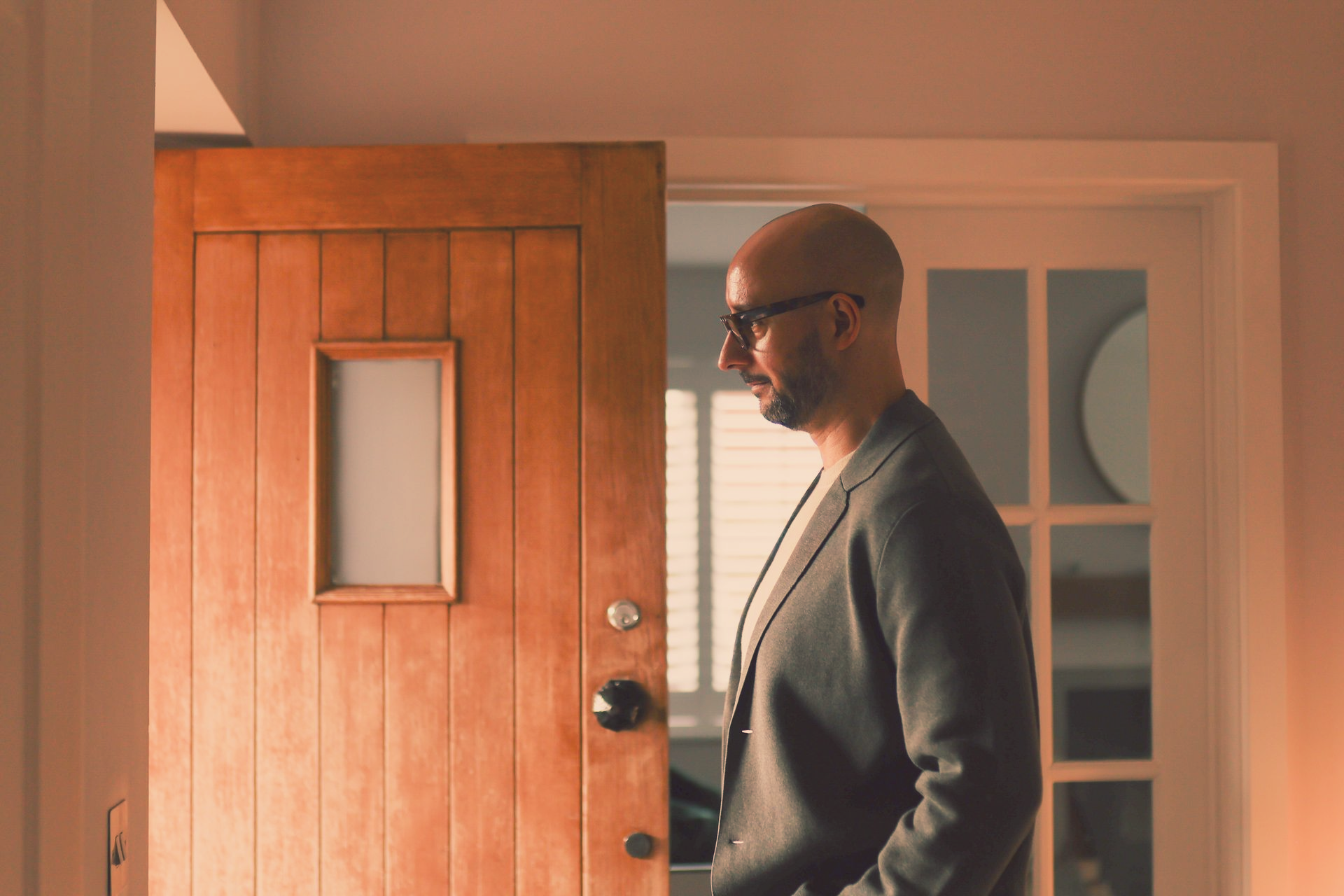 Justin Tate of The Exec Memo  in a gray blazer stands near an open wooden door and a glass-paned door. Interior, neutral lighting.