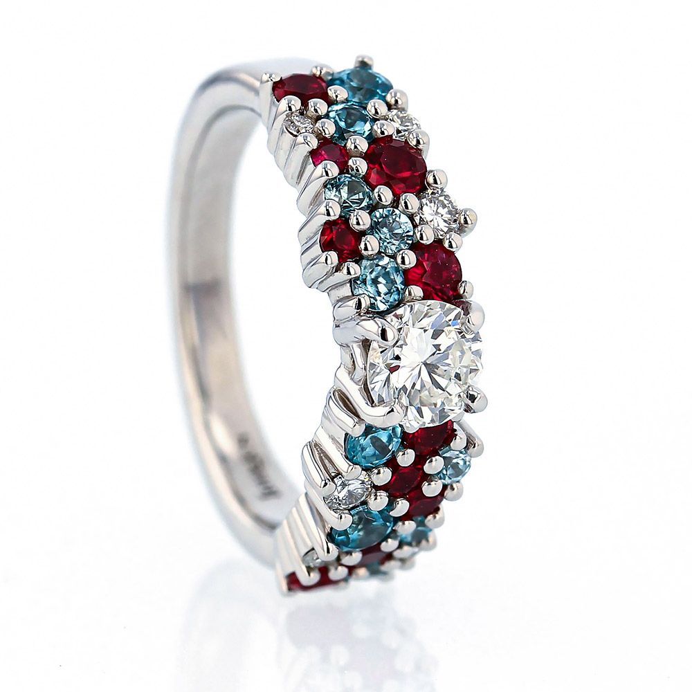 White gold diamond ring set with a large round diamond in the center with 10 small rubies, 10 small blue zircons, and 6 small diamonds.