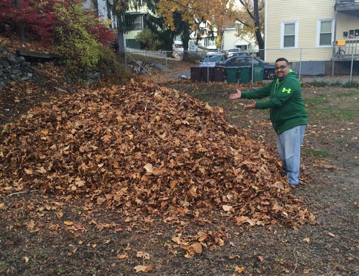 A man in a green jacket is standing in front of a pile of leaves.