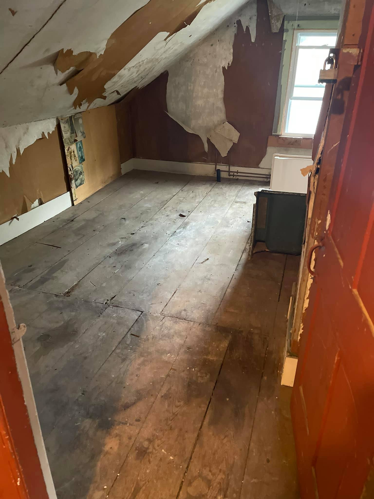 An empty room with a wooden floor and a red door.