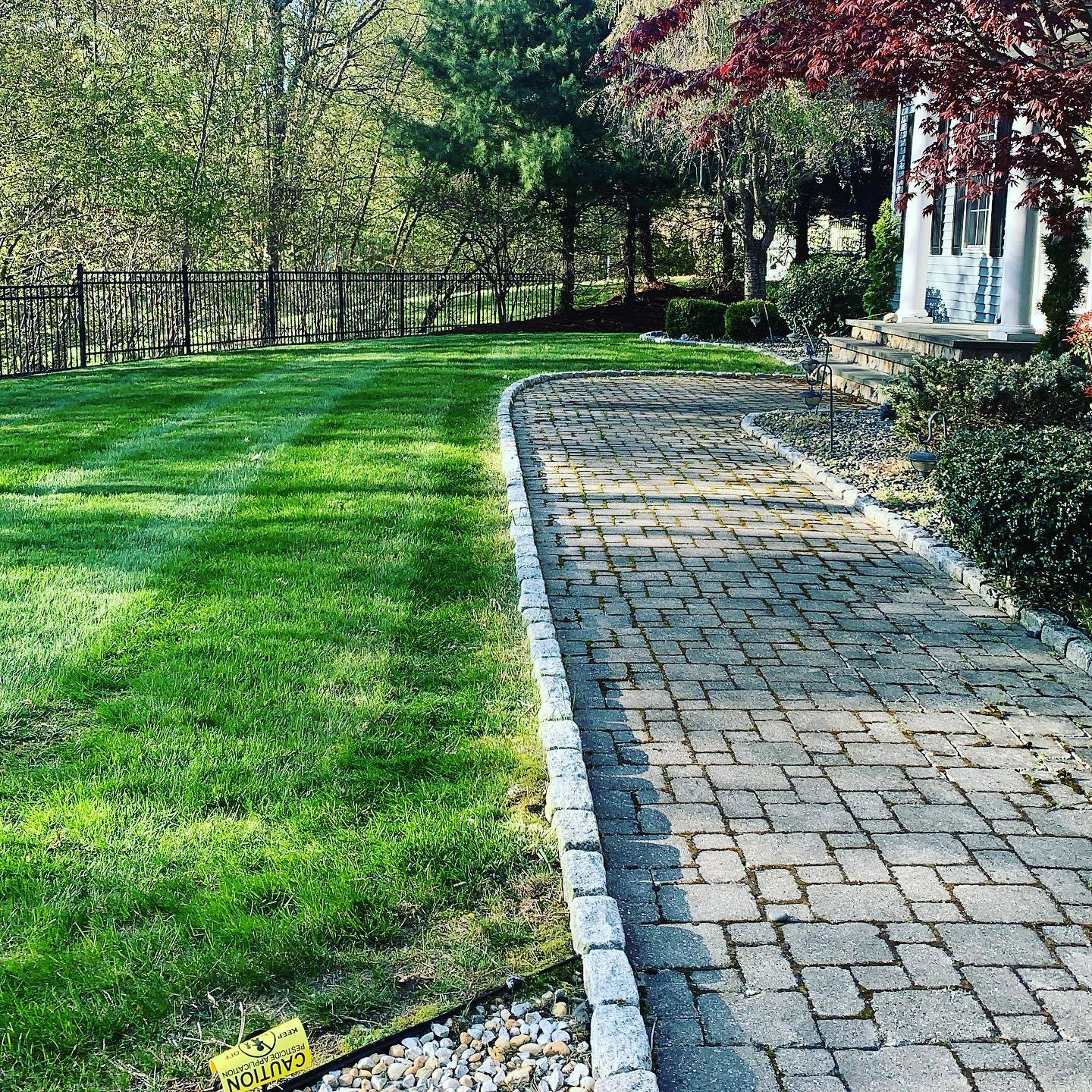 A brick walkway leading to a house with a lush green lawn.