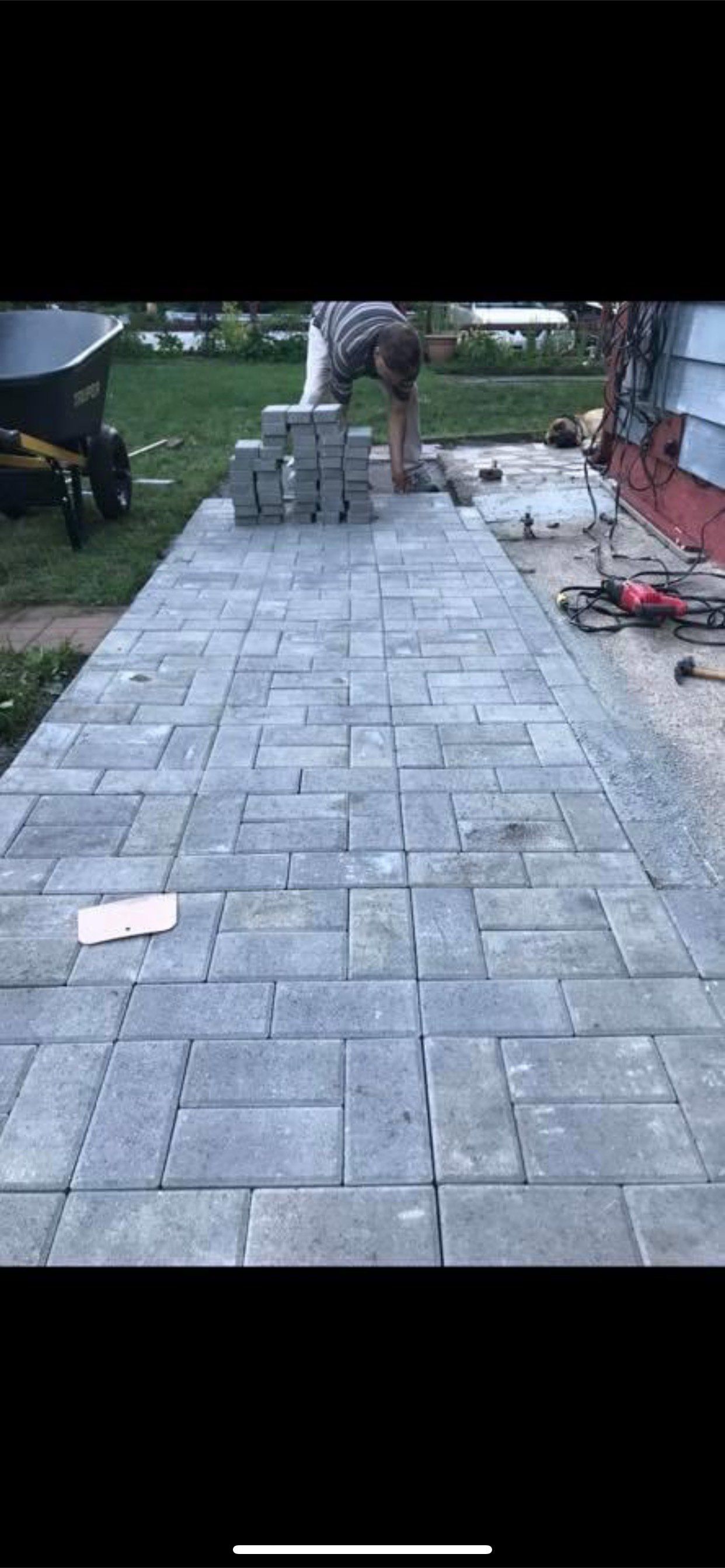 A man is laying bricks on a sidewalk in front of a house.