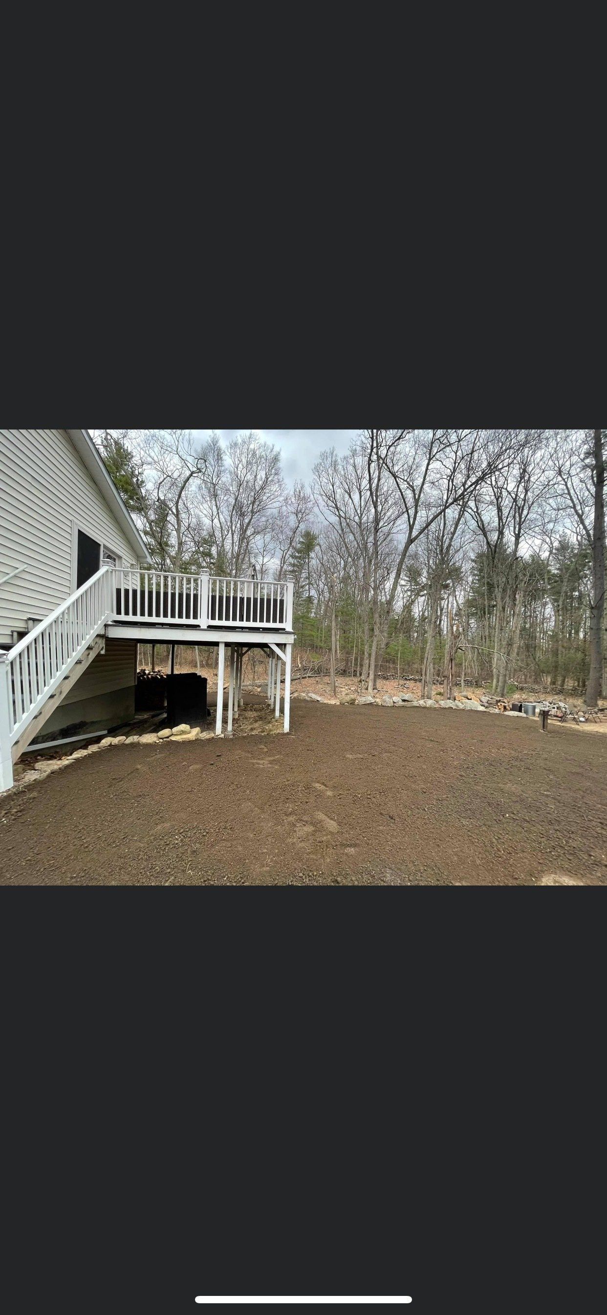 A white deck with stairs leading up to it is in the backyard of a house.