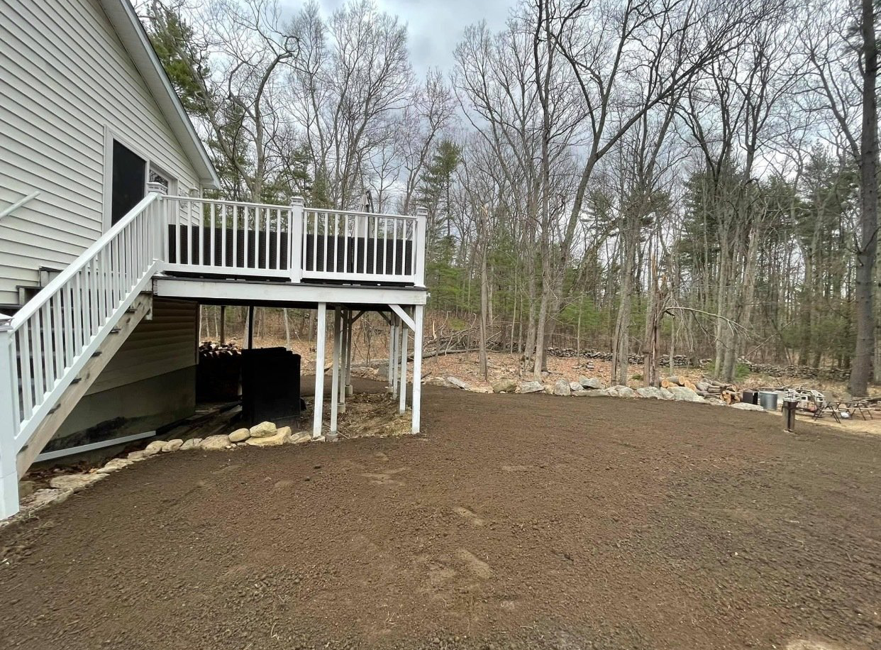 The backyard of a house with a large deck and stairs leading up to it.