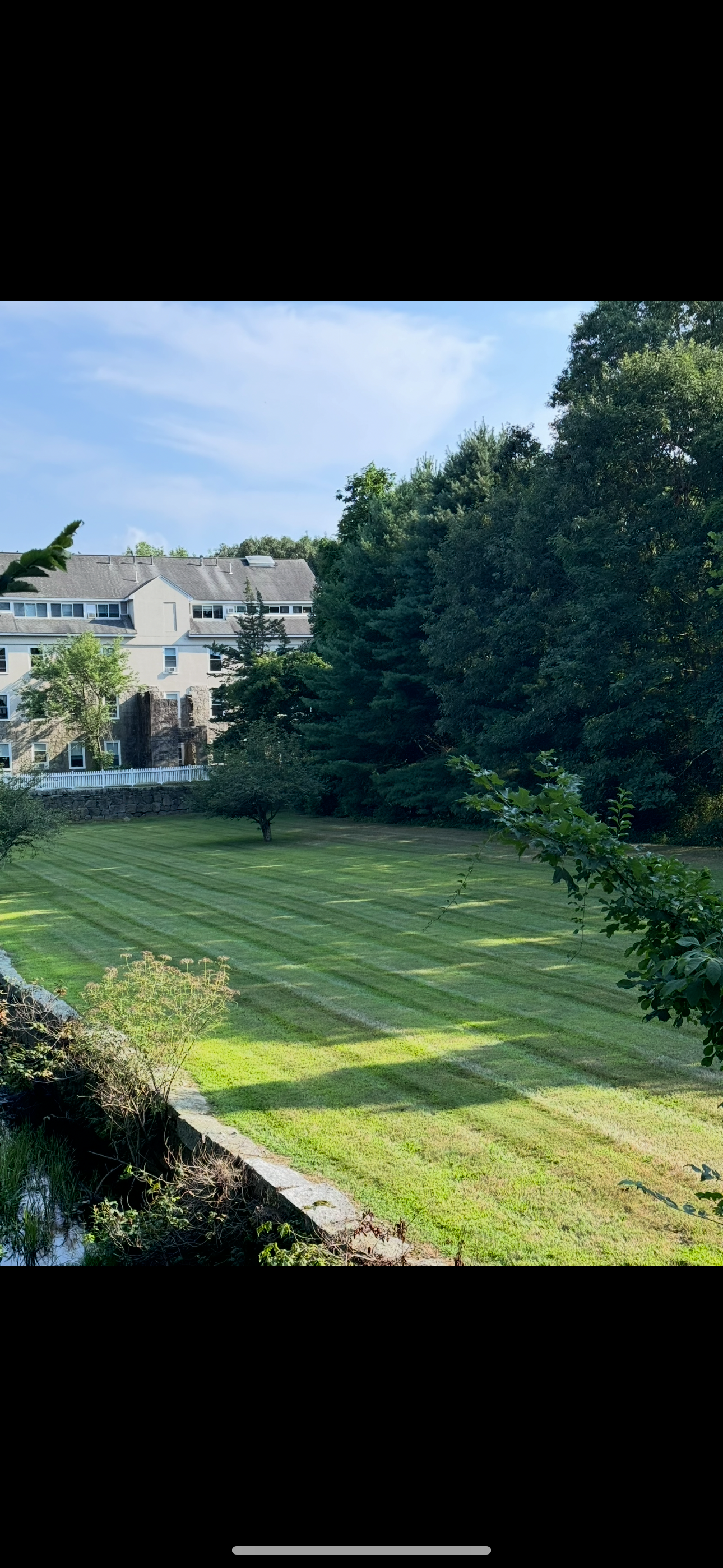 A large grassy field with trees in the background and a house in the background.