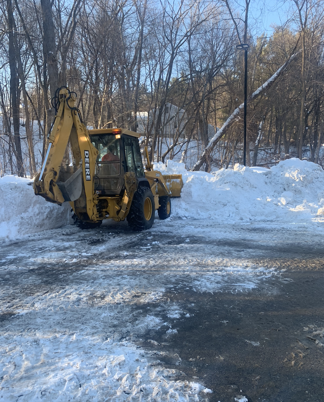 A yellow backhoe is clearing snow from a parking lot.