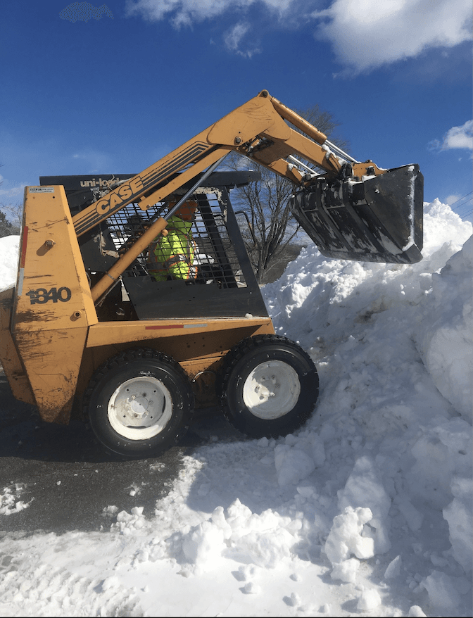 A man is driving a case skid steer through a pile of snow.