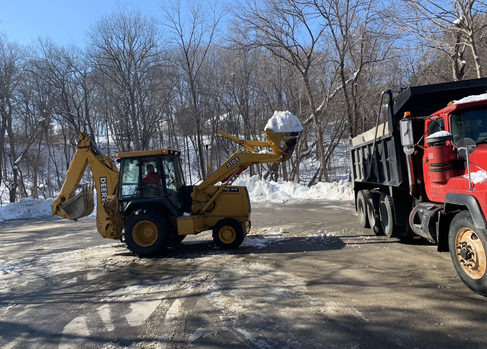 A yellow excavator is loading snow into a dump truck.