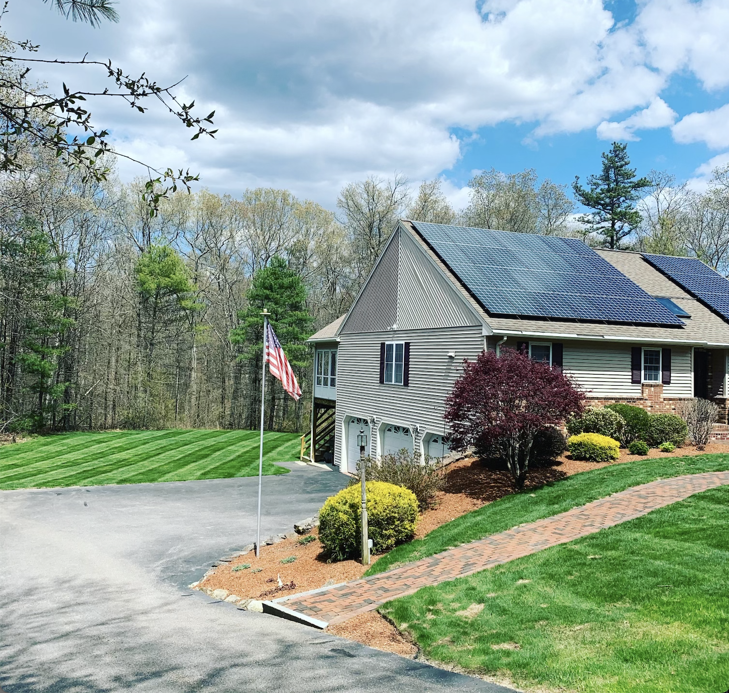 A house with solar panels on the roof is surrounded by trees and grass.