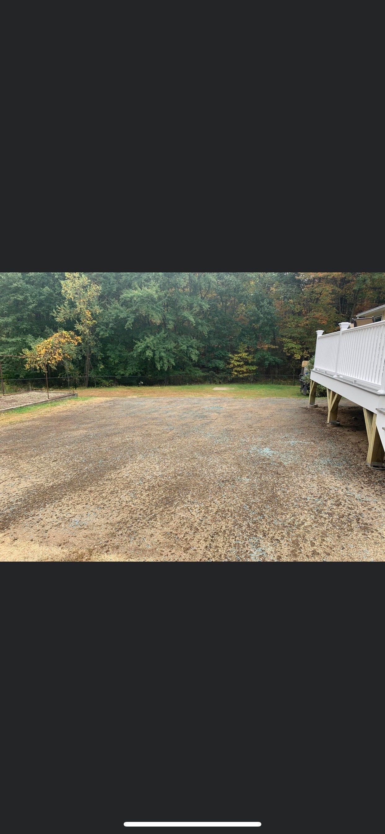 A large empty yard with a white fence and trees in the background.