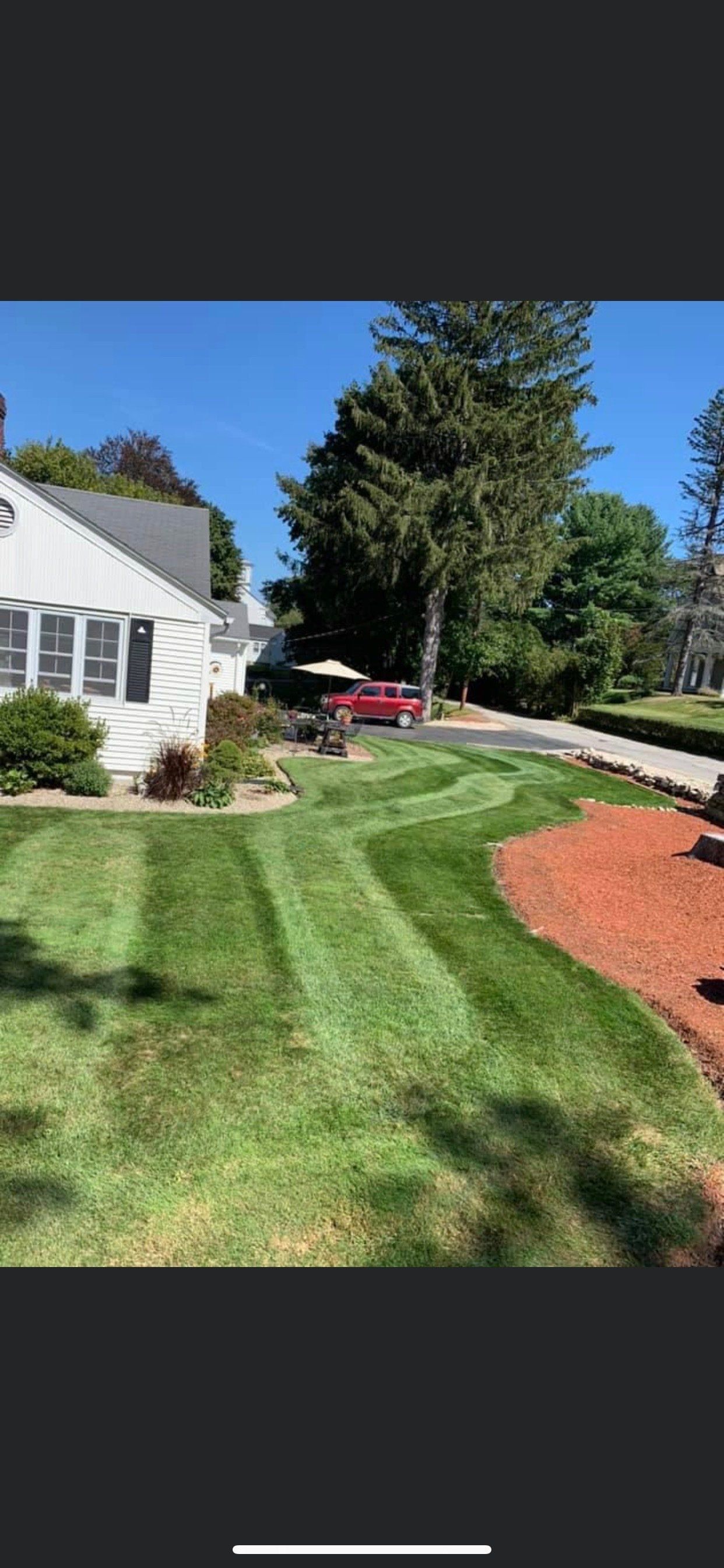 A house with a lush green lawn and a red car parked in front of it.