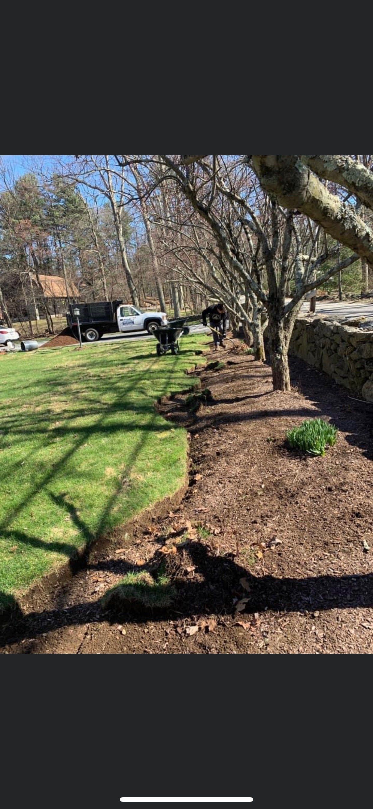 A lawn with a truck parked in the background and a pile of mulch in the foreground.