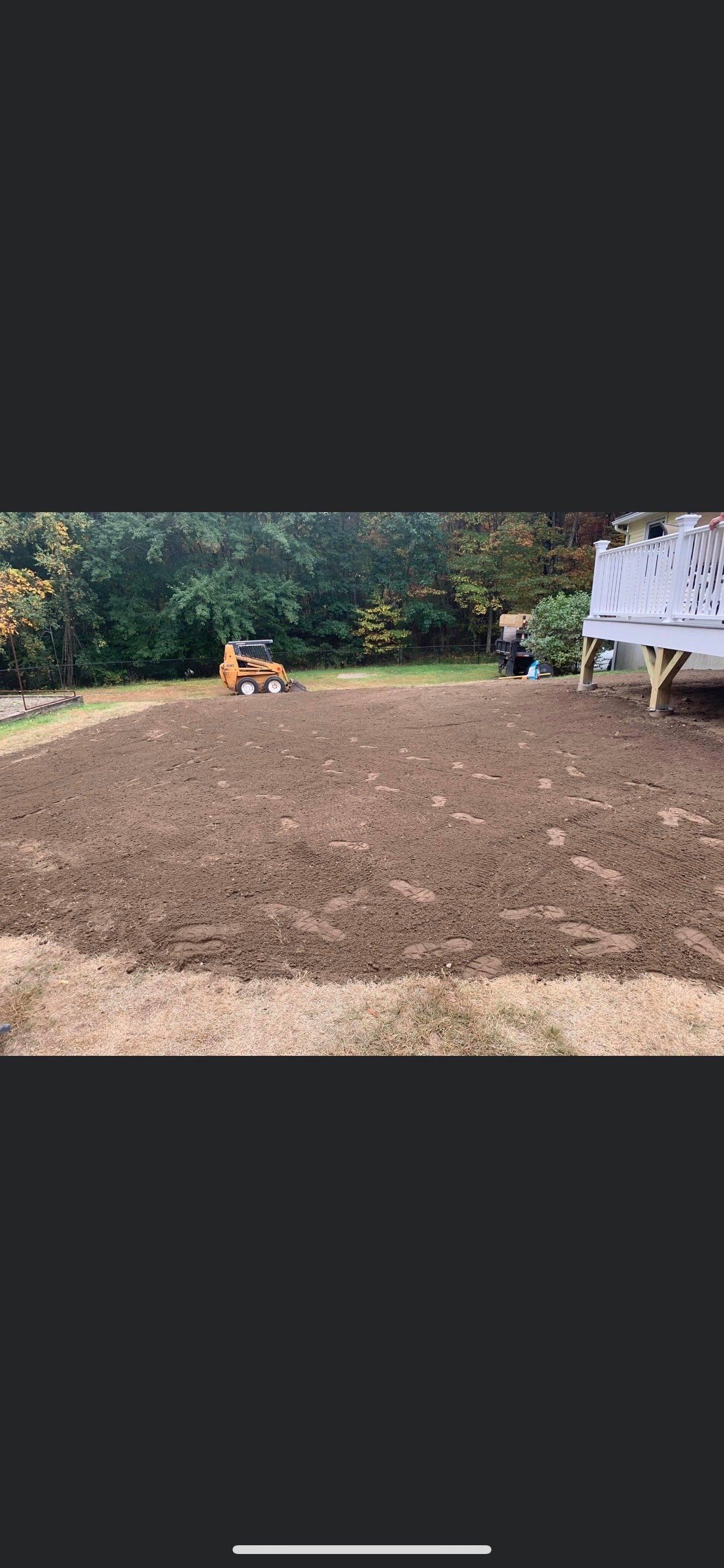 A bulldozer is plowing a dirt field in a backyard.